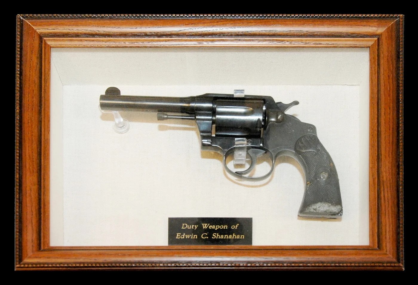 A revolver mounted in a frame beside a plaque reading Duty Weapon of Edwin C. Shanahan.