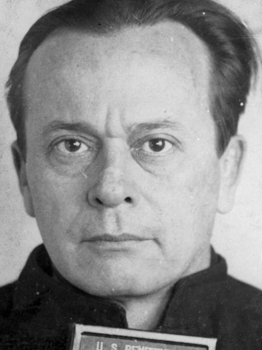 Close head-and-shoulders photograph of Arthur Barker, a balding man looking straight at the camera, with the top of a U.S. Penitentiary placard at the bottom edge.