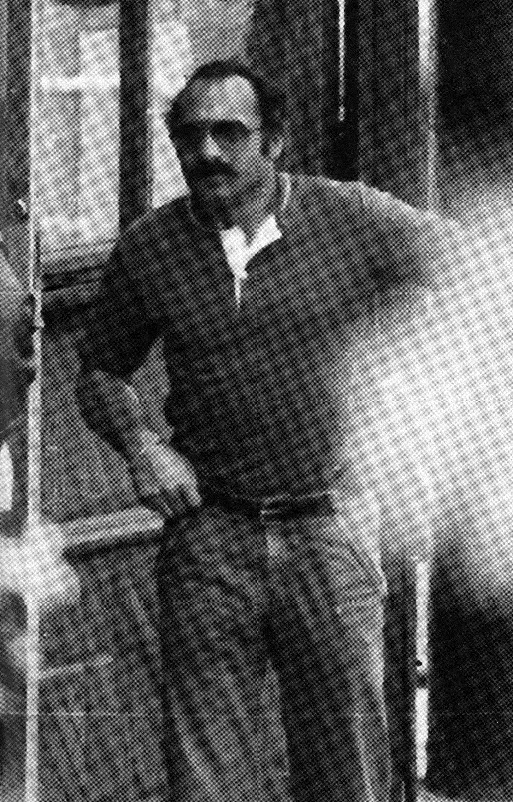 Undercover agent Joe Pistone: full-length photograph of a man in sunglasses and a dark short-sleeved shirt, standing in a doorway with one hand on his hip; the right side of the frame is washed out by glare.