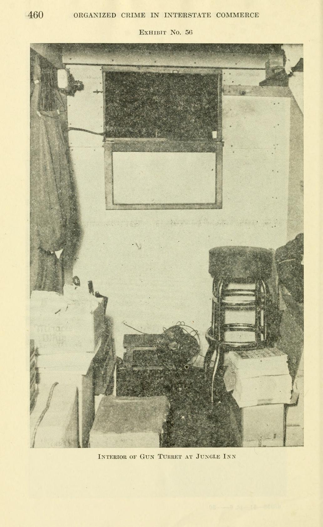 Exhibit No. 56, a photograph of a cramped room with a chair, a window slot, cables and boxes on the floor, captioned "Interior of Gun Turret at Jungle Inn".