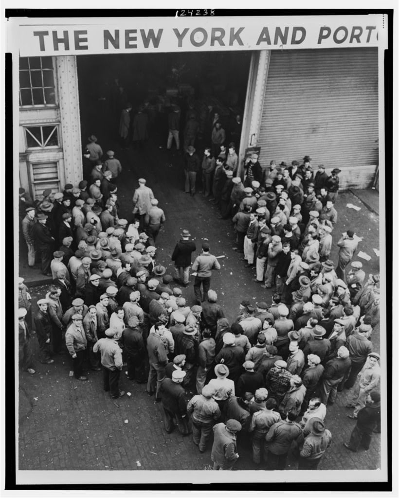 High-angle view of a large crowd of men gathered in a pier shed under a sign.