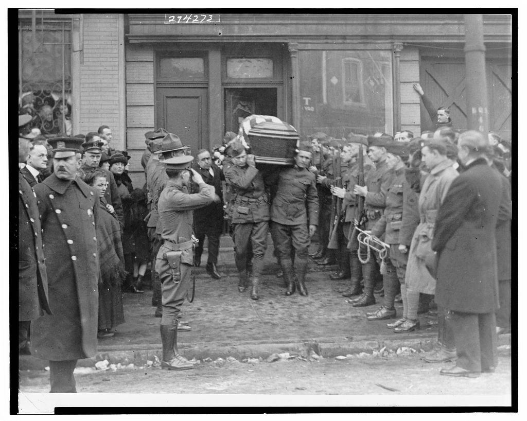 Soldiers carrying a coffin past a line of men in uniform, with a crowd of onlookers, December 1920.