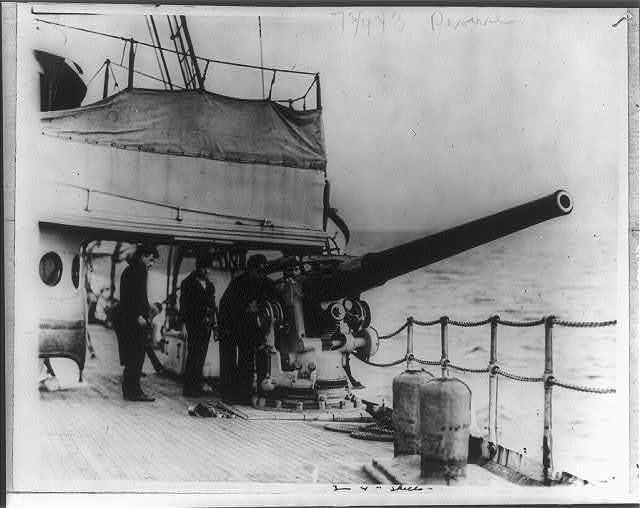 Four Coast Guardsmen on deck beside a four-inch cannon.