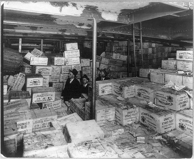 Prohibition agents among stacked cases of Scotch whiskey in the hold of a captured ship.