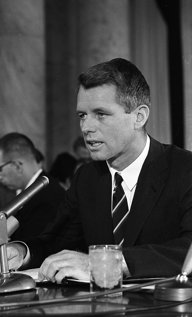 Robert F. Kennedy speaking at a witness table with a microphone and a glass of water, 25 September 1963.