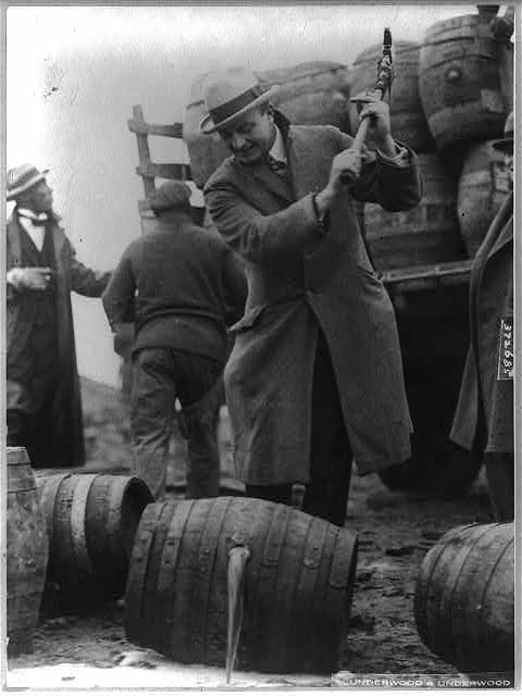 Barrels of beer being emptied into the Schuylkill River, with a man swinging an axe.