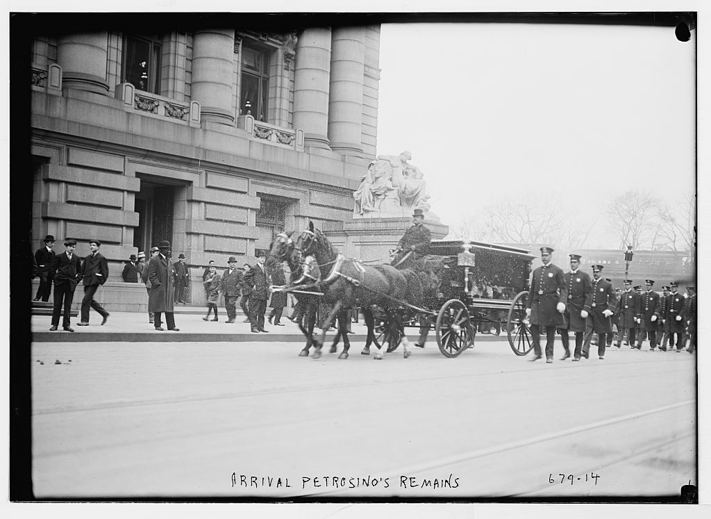 A two-horse hearse passes a columned stone building, followed by a column of uniformed police officers; the negative is captioned 'Arrival Petrosino's remains'.