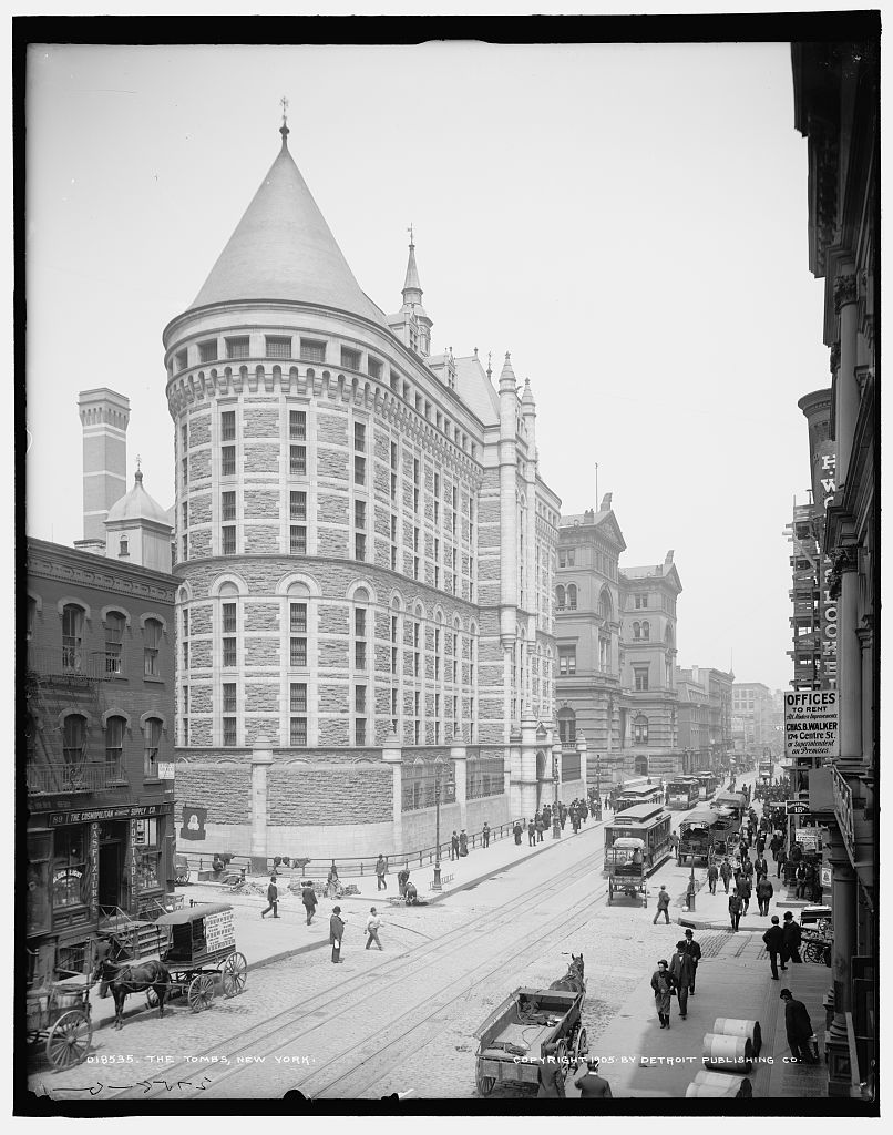 Exterior view of the Tombs prison building in New York, with a street at the right edge of the frame.