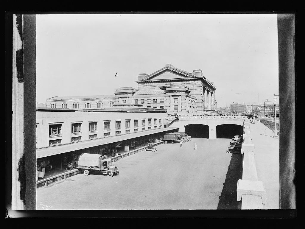 A black-and-white photograph of Kansas City Union Station and its loading dock with trucks and automobiles in the foreground