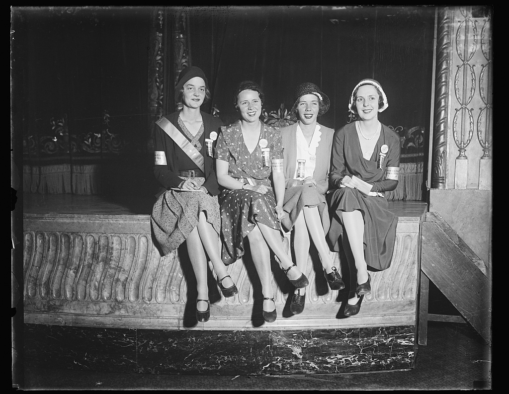 Four women seated in a row wearing sashes.