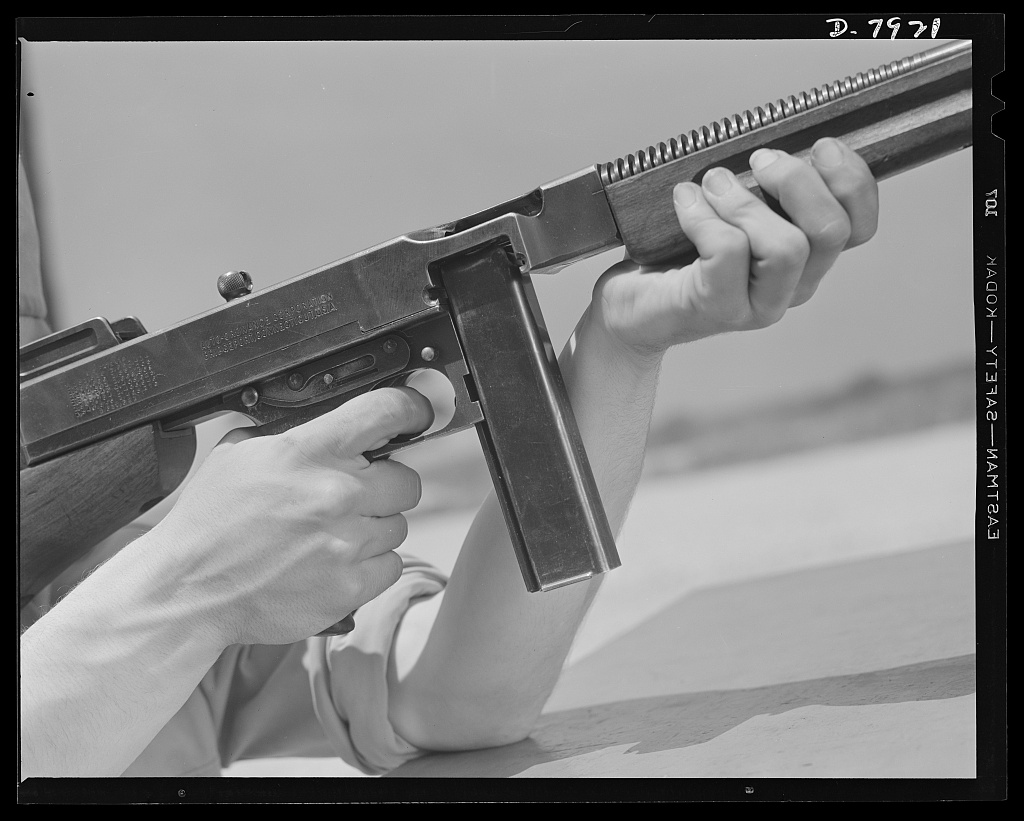 Close view of a person's hands holding a Thompson submachine gun with a box magazine.