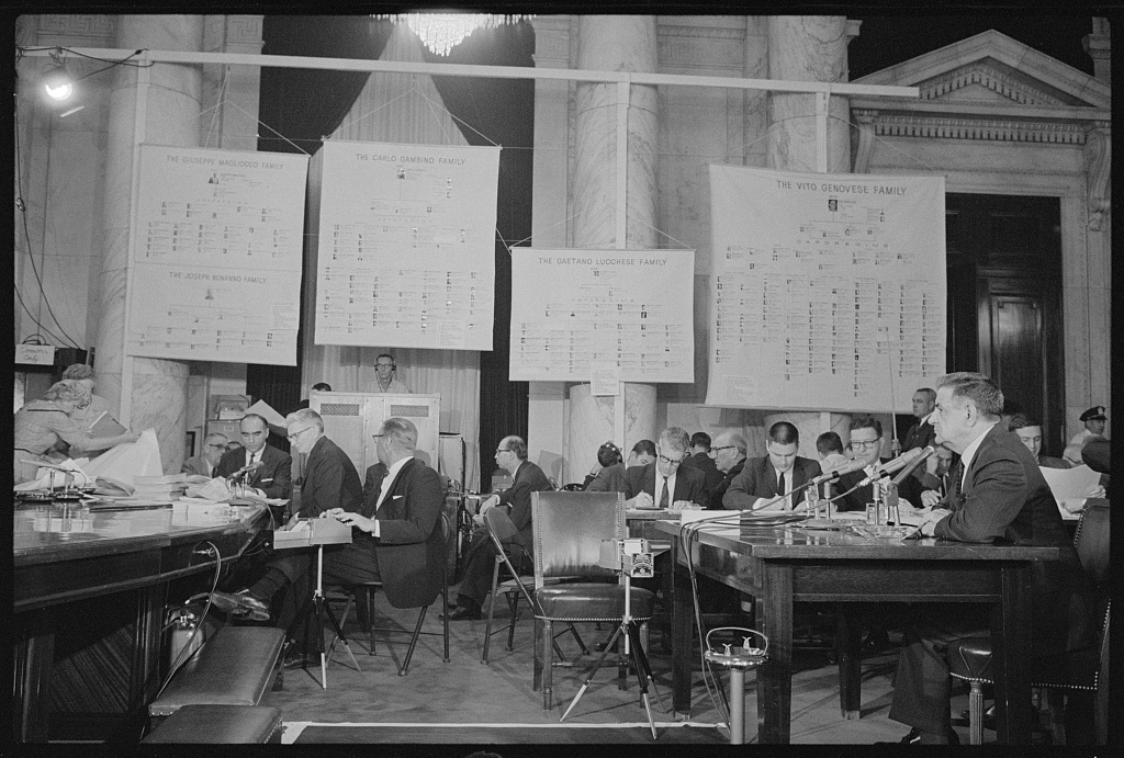 Joseph Valachi testifying at a Senate subcommittee hearing, with charts hanging in the room, 8 October 1963.