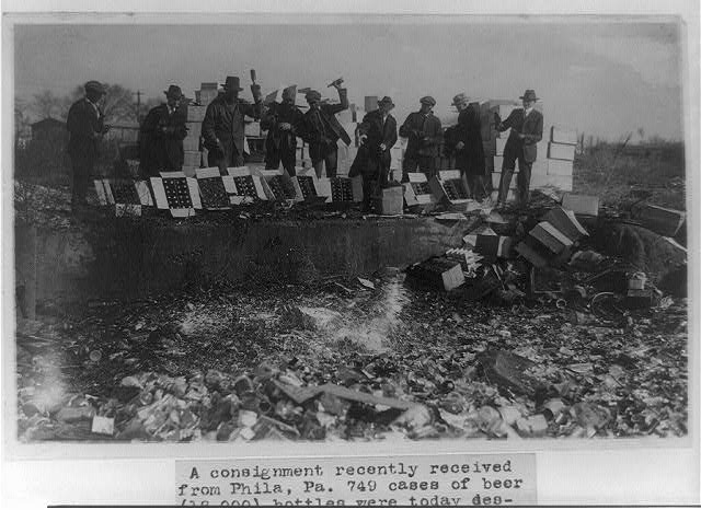 Nine men smashing bottles at a dump.
