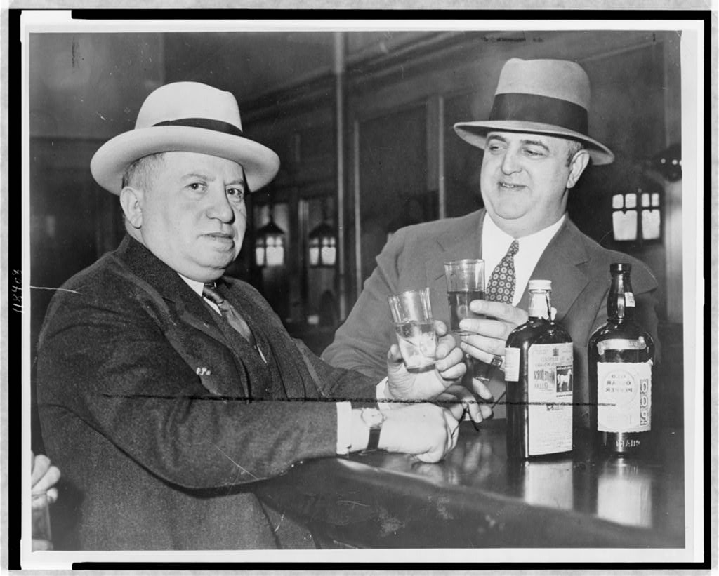 Two men in suits raising glasses together at a bar.