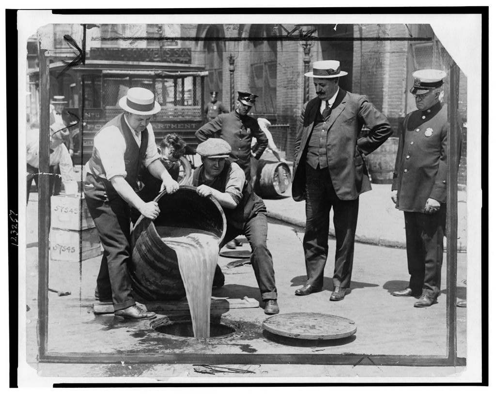 Agents pouring liquor into a sewer after a raid while New York City Deputy Police Commissioner John A. Leach watches from the right.
