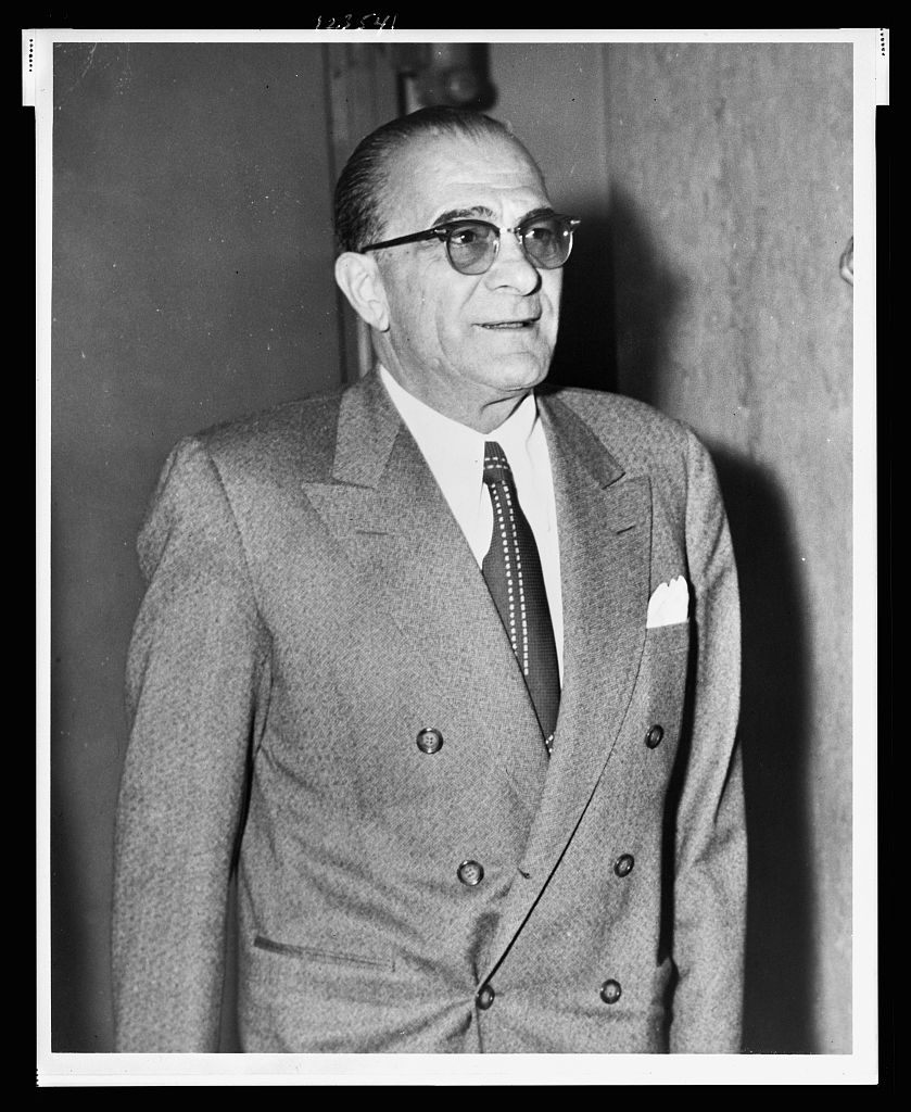 Half-length photograph of Vito Genovese standing, facing right.