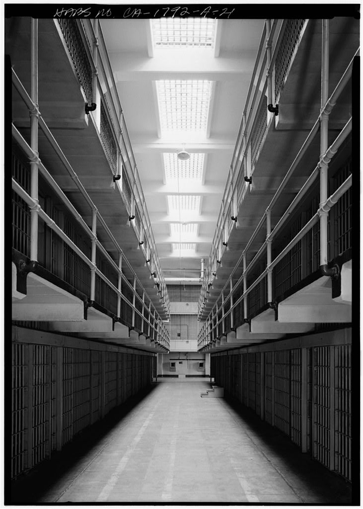 Black-and-white HABS photograph looking down the central aisle of the Alcatraz cell house between two blocks of cells, with a skylit ceiling.