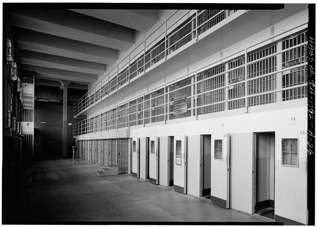 Black-and-white HABS photograph of a long gallery of solid-fronted cell doors in Cell Block D at Alcatraz, with a tier of cells above.