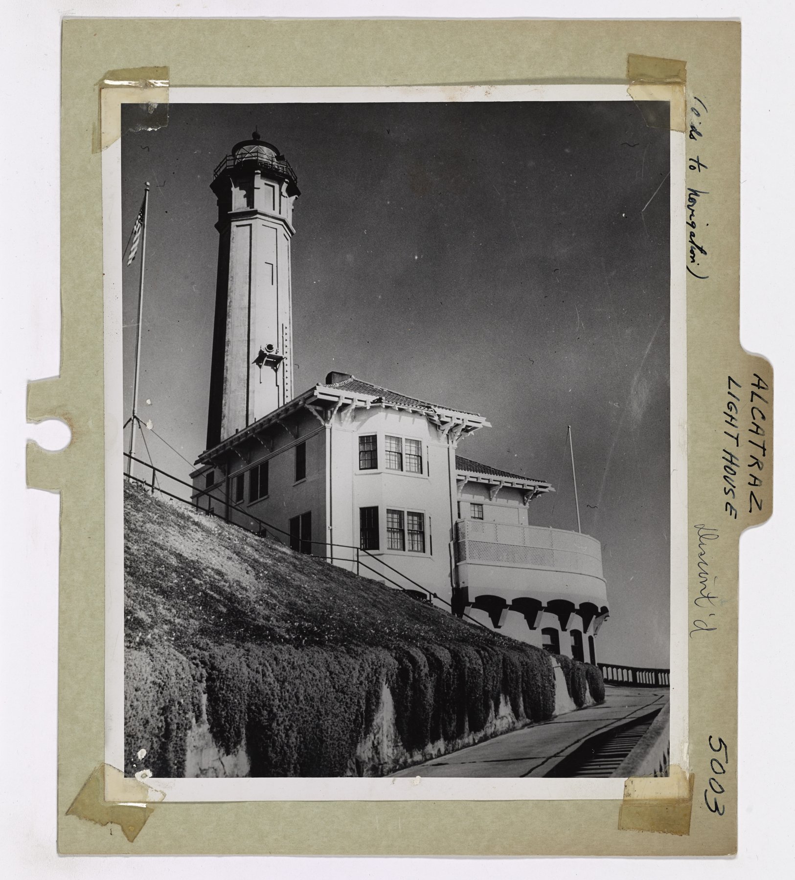 Mounted print of a tall square lighthouse tower and a two-storey house on a slope with hedges and a flagpole flying the U.S. flag; handwriting on the mount reads Alcatraz Light House.