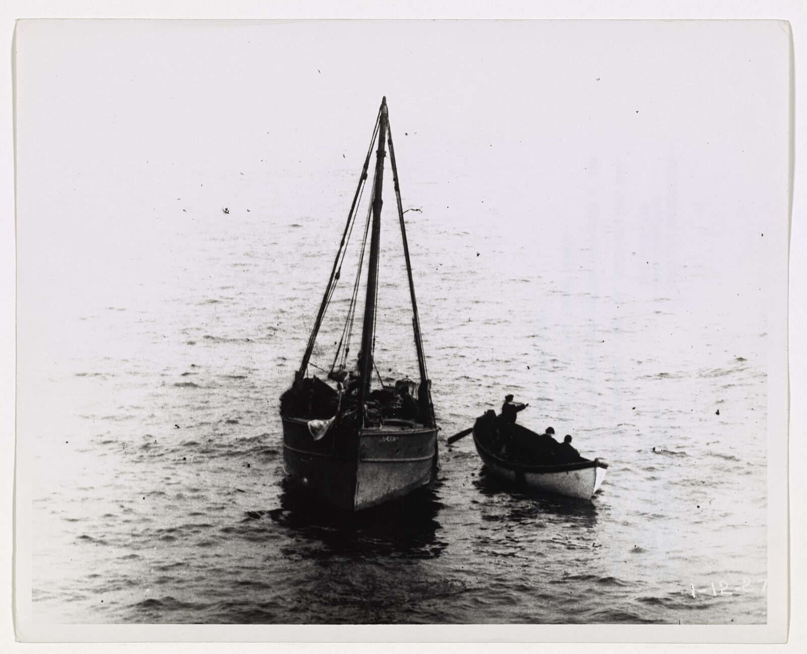 A two-masted vessel with a small boat of men alongside it.