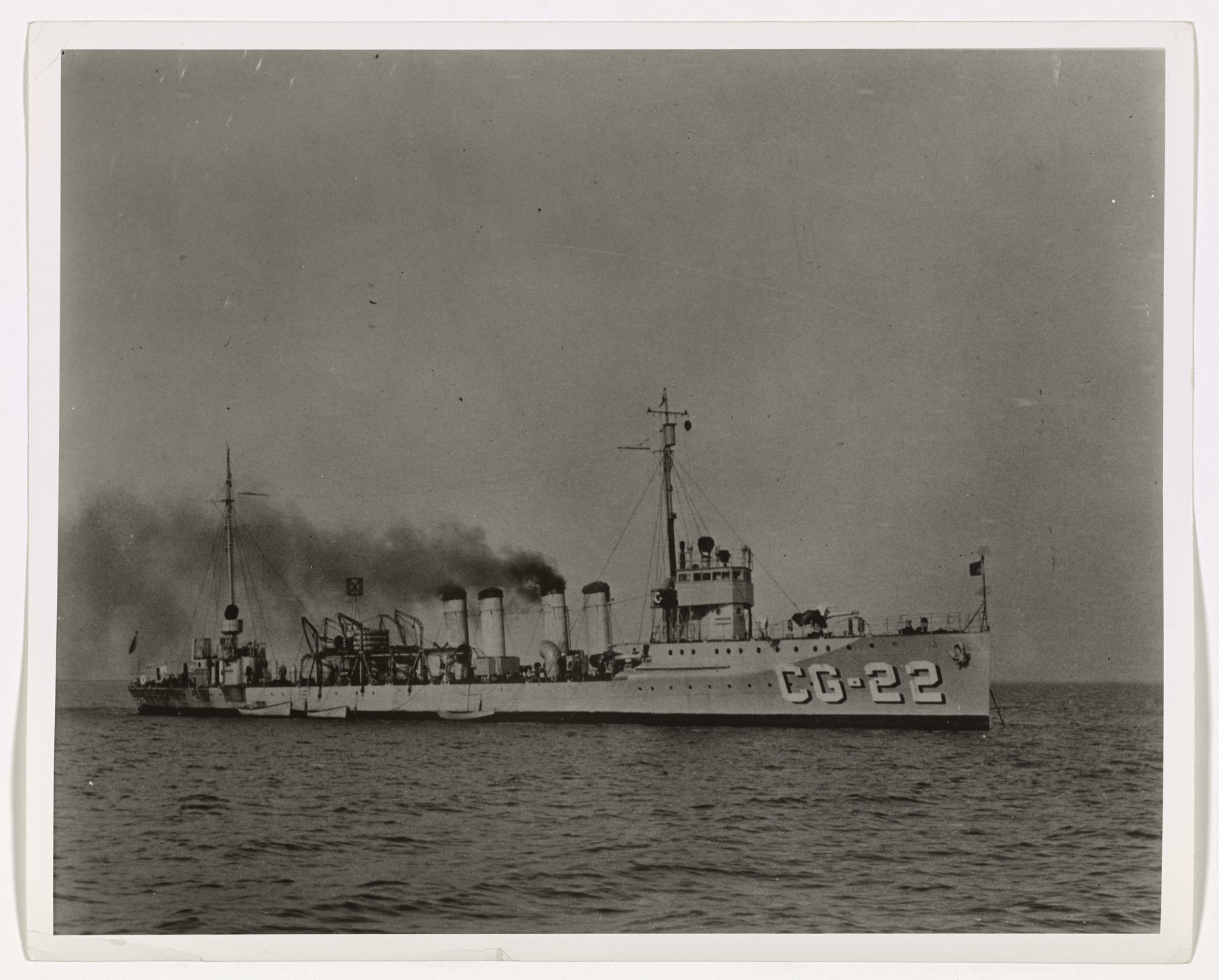 A four-stack destroyer broadside at sea with hull number CG-22 and heavy black smoke from her funnels.