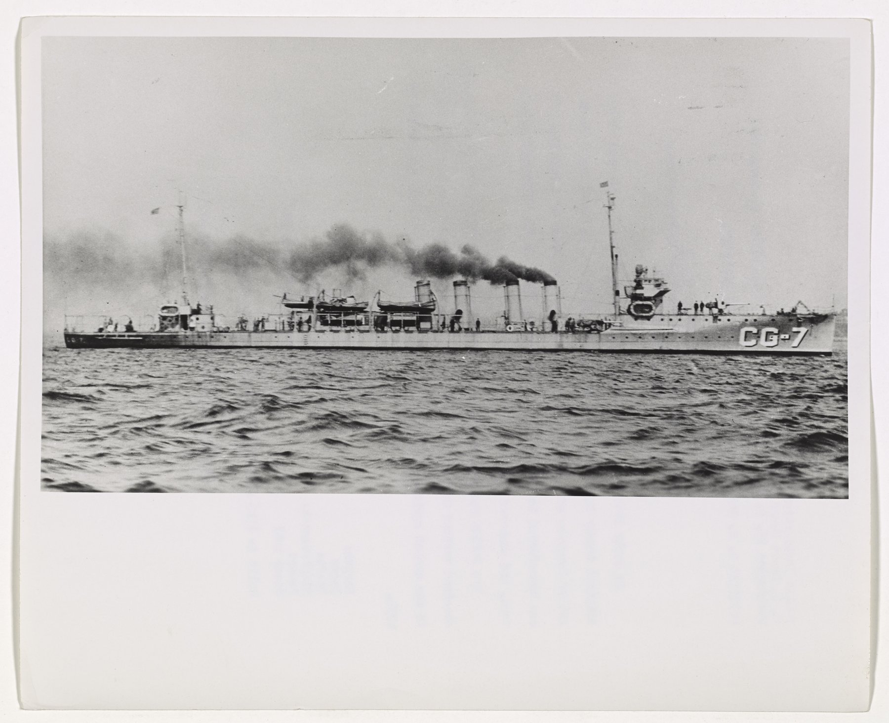 A four-stack destroyer broadside at sea with hull number CG-7 and black smoke from her funnels.