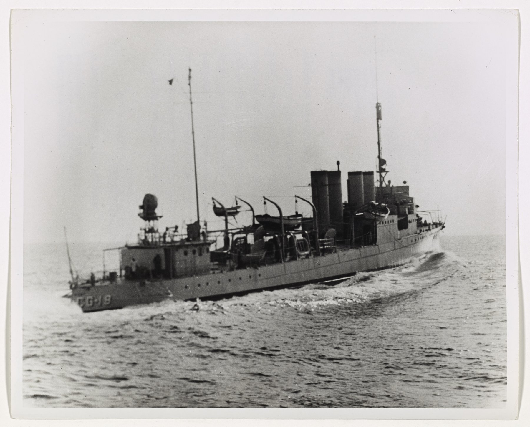 A four-stack destroyer seen from astern under way, hull number CG-18 on the stern and boats in davits.