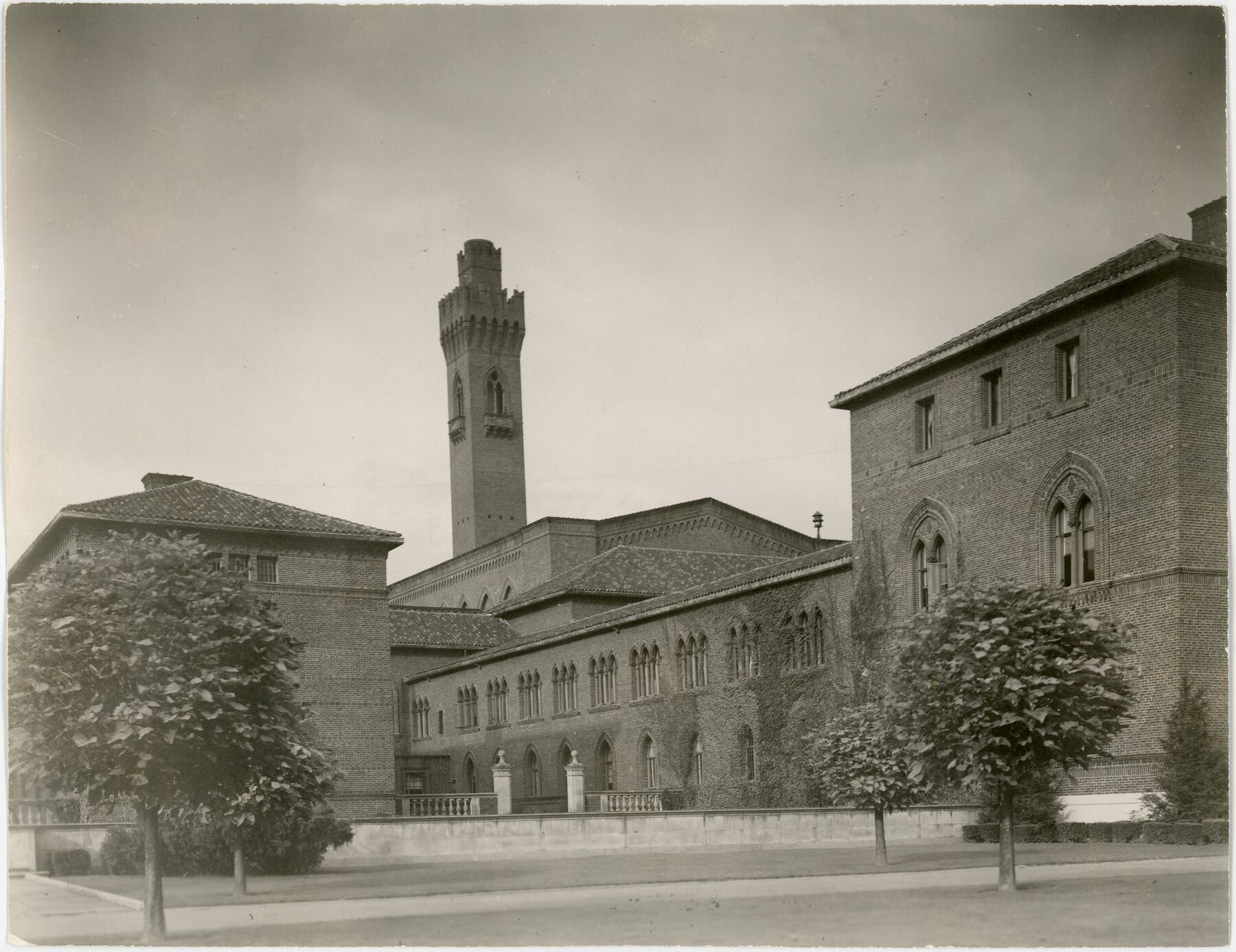 Sepia photograph of a brick penitentiary building with tall windows, a tall tower and trees in front, seen from the street.