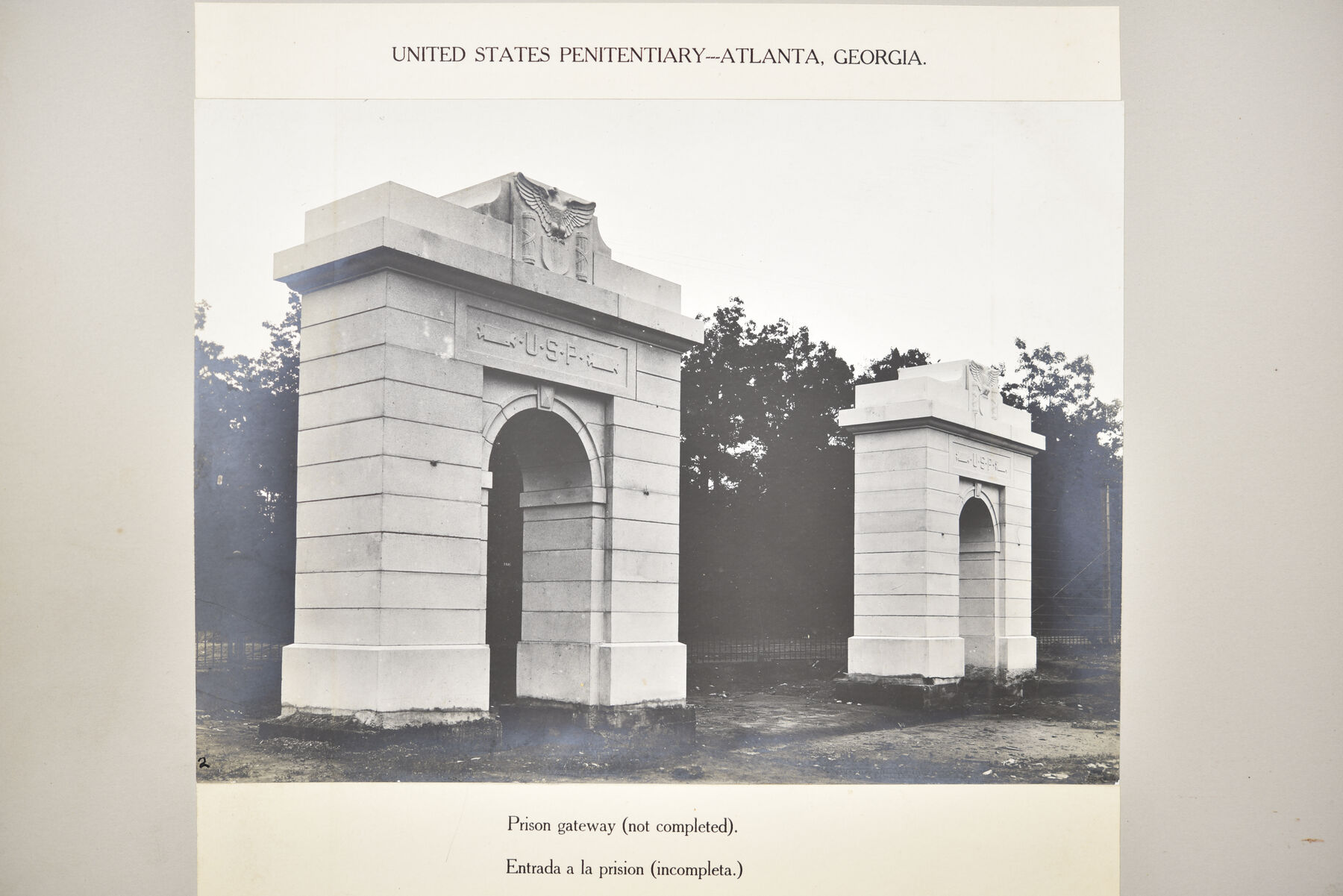 Mounted photograph of a tall stone gateway arch lettered USP with a smaller arch beside it, among trees.