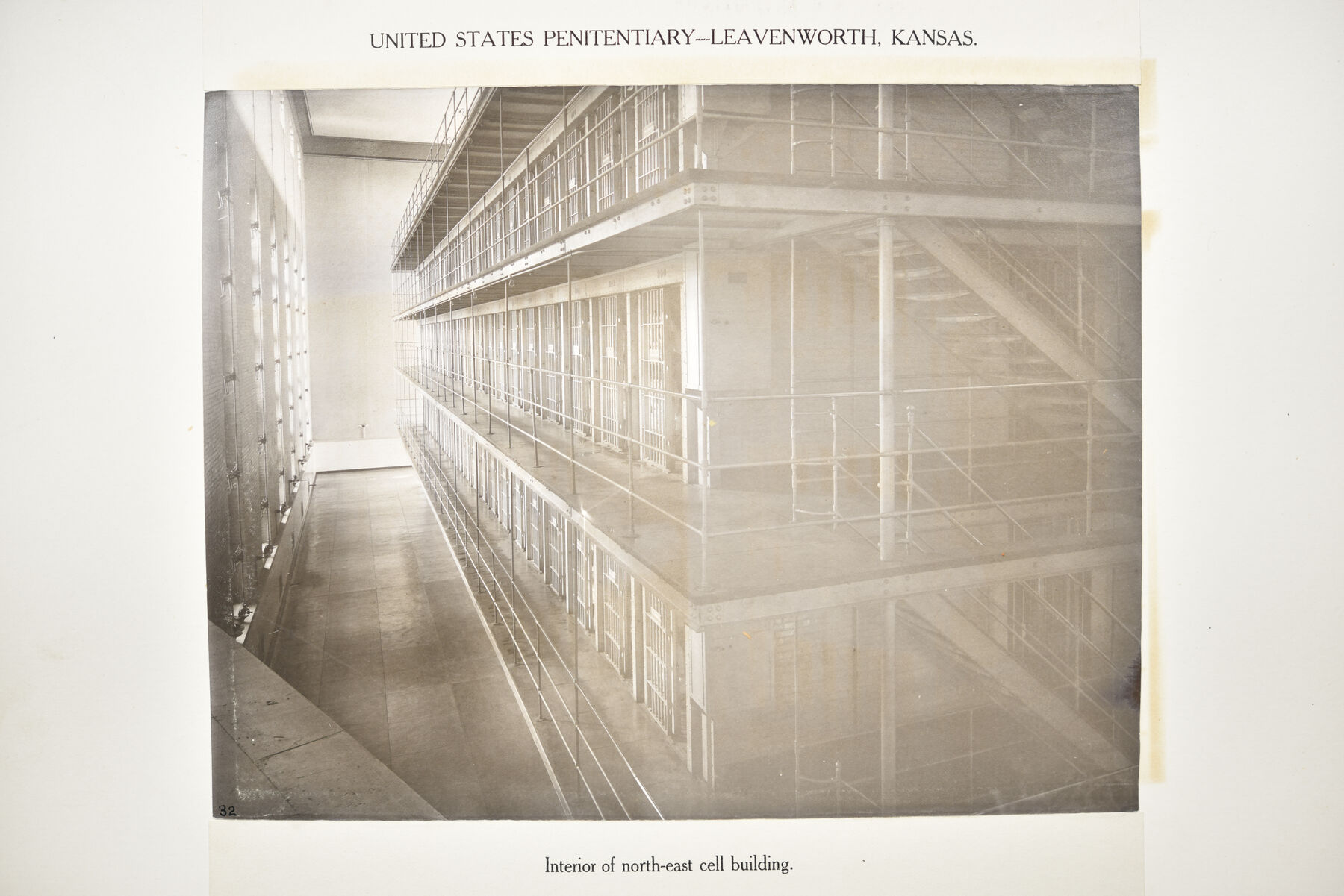 Sepia mounted photograph of the interior of a Leavenworth cell building with several tiers of cells and galleries receding down a long hall.